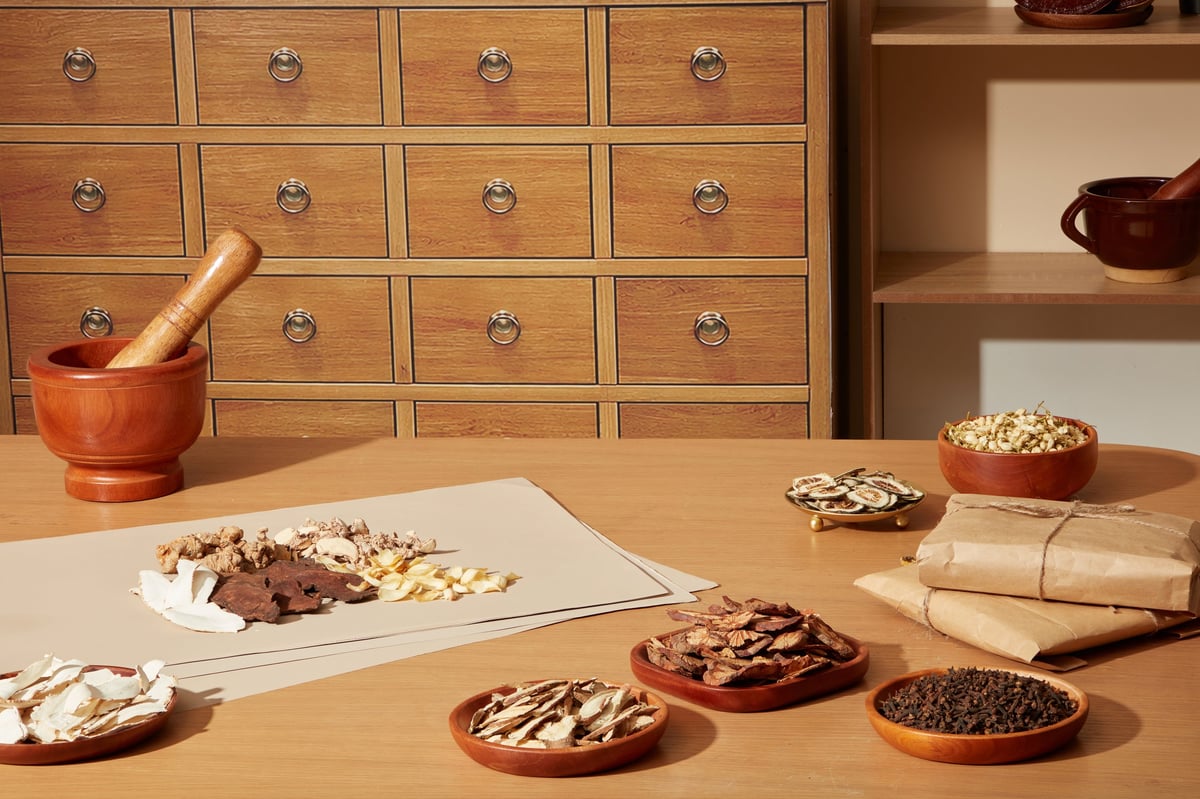 Dried herbal ingredients arranged on paper with mortar and bowls. Scene showing preparation of traditional herbal prescription in oriental medicine apothecary.