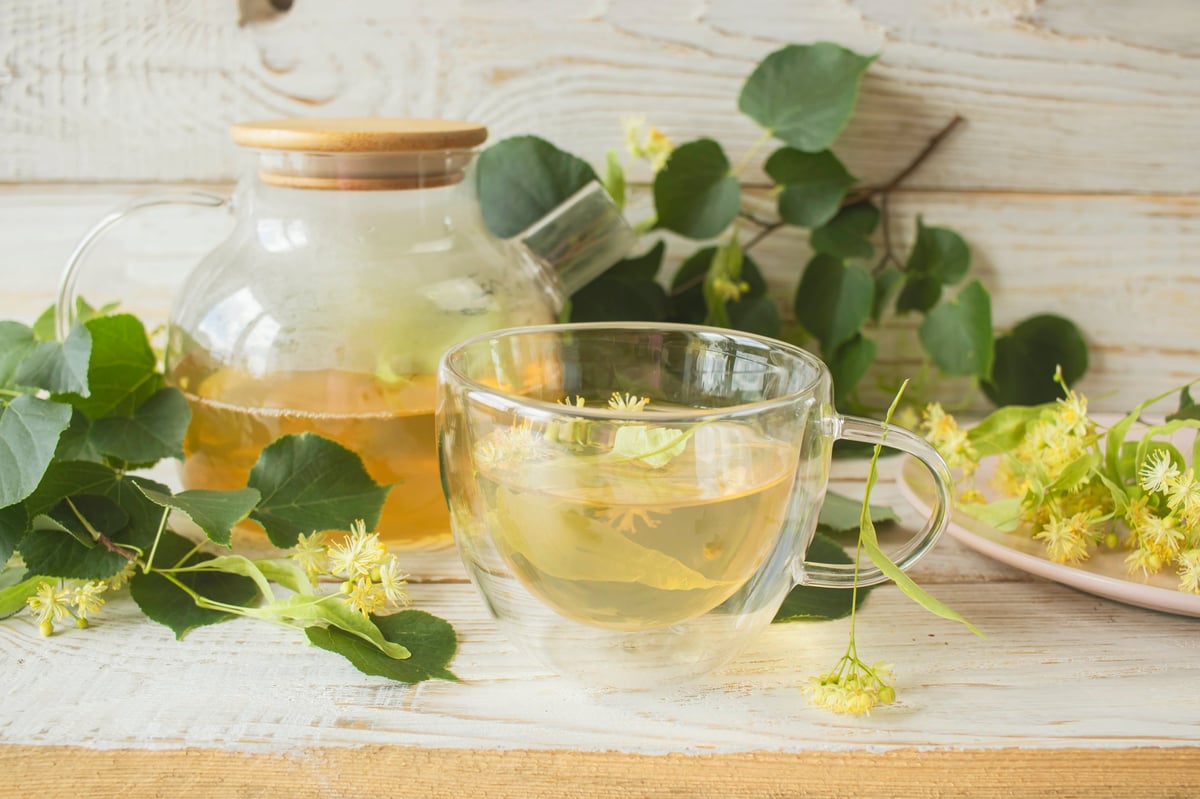 Linden tea in a glass cup with fresh linden flowers, on a wooden background. Medicinal herbal tea.