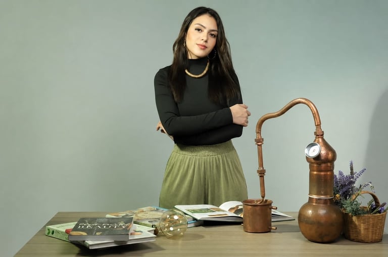 Woman in black top and olive skirt standing at desk with magazines, brass lamp, wooden pitcher, and lavender plant